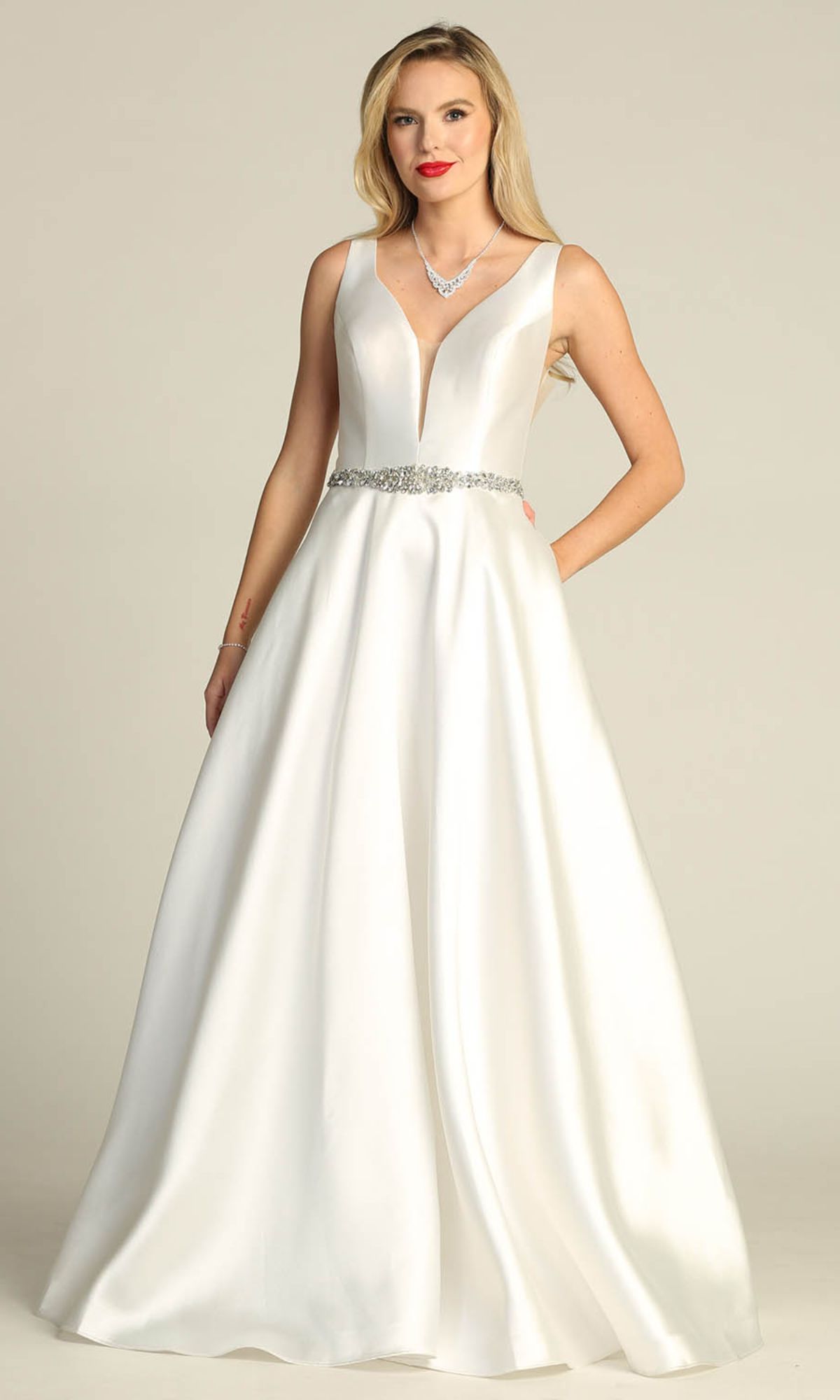 A woman wears the Jeweled-Waist Long Prom Ball Gown Chicas CC3021, a sleeveless white A-line dress with a deep V-neckline and jeweled belt, standing against a plain background.